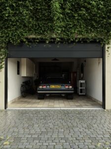 A classic car parked in an ivy-covered garage with a cobblestone driveway, exuding a retro charm.