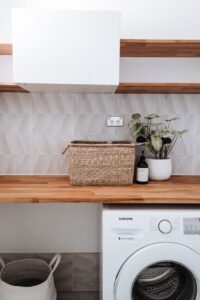 Interior of modern apartment with washer near container under wicker basket placed near potted plant and bottle of soap
